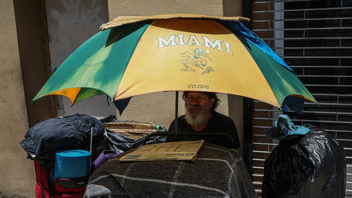 Una persona sin hogar se sienta a la sombra de una sombrilla durante una ola de calor en Miami
